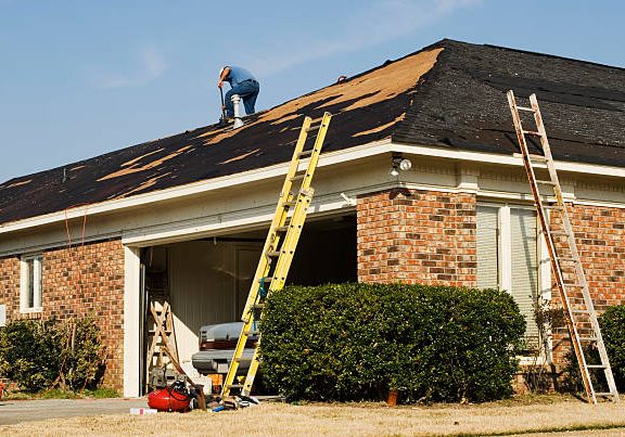 Mexican ethnicity construction male worker is on a rooftop repairing shingles that were destroyed due to an EF2 tornado. With his back turned he is unrecognizable. An EF2 tornado came through this residential neighborhood in Columbus Georgia in the early spring and destroyed many houses and roofs.